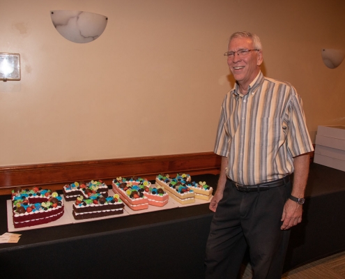 Past Executive Director standing by cake letters that spell his name.